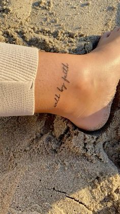 a person's foot in the sand with a small tattoo on their left leg