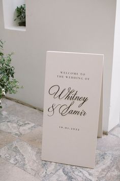 a welcome sign on the ground next to a potted plant in front of a white wall