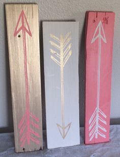 three wooden signs with arrows painted on them, one is pink and the other is white