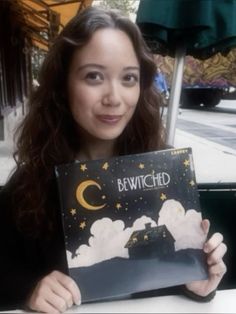 a woman holding up a book with the words bewitched written on it in front of her face