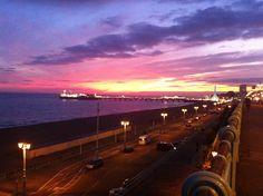 the sun is setting over the ocean and cars are parked on the side of the road