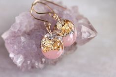 two pink and gold earrings sitting on top of a piece of rock next to crystals