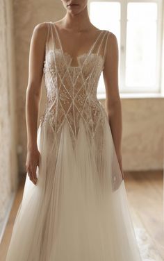 a woman in a wedding dress is standing near a window and looking down at the floor