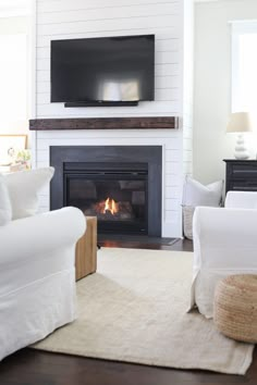 a living room with white furniture and a flat screen tv above the fireplace