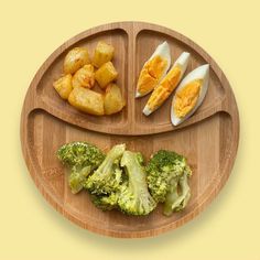 a wooden plate with broccoli, eggs and potatoes on it in the shape of a smiley face