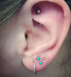 an ear piercing with three different colored stones on the top and bottom of each ear