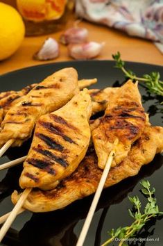 chicken skewers on a black plate with lemons in the background