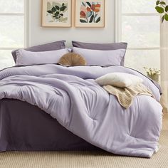 a bed with purple sheets and pillows in front of two framed pictures on the wall