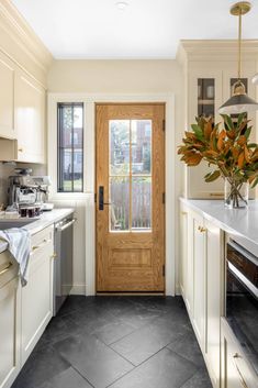 a kitchen with white cabinets and black flooring next to a wooden door that leads to an outdoor deck