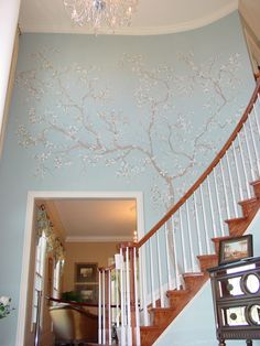 the stairs are decorated with white flowers and branches painted on the wall above them, along with a chandelier