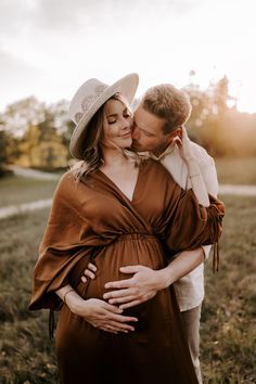 a pregnant couple cuddles in a field at sunset