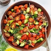 a wooden bowl filled with cucumber, tomatoes and onion salad next to lemon wedges