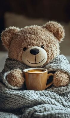 a teddy bear wrapped in a blanket with a cup of coffee sitting on top of it