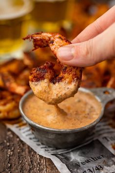 a person dipping some kind of food into a small metal bowl with sauce in it