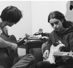 two people sitting on a couch with guitars in their hands and one person playing the guitar