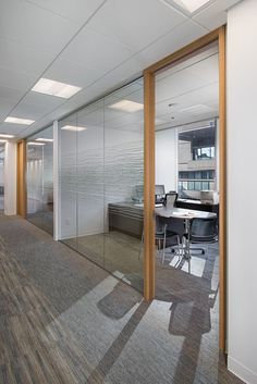 an empty office with glass walls and wood trimmings on the wall, along with chairs and desks