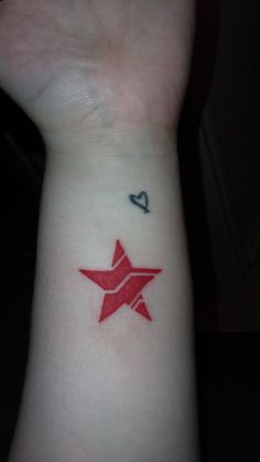 a red star tattoo on the wrist with a small black dot in the middle and an arrow at the bottom