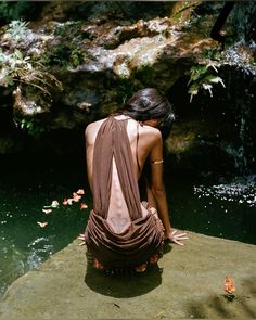 a woman sitting on top of a rock next to a body of water with goldfish in it