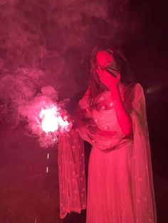 a woman dressed in red holding a lit up firecracker while standing next to her face