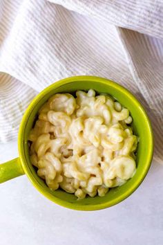 a green cup filled with macaroni and cheese on top of a white cloth