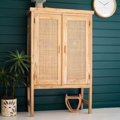 a tall wooden cabinet sitting next to a clock on a green wall and potted plant