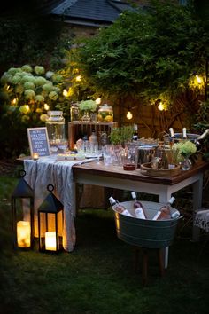 an outdoor dinner table with candles and lights on the outside, surrounded by greenery