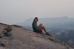 a woman sitting on top of a large rock