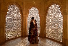 two people standing next to each other in front of large windows with carved screens on them