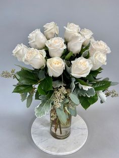 a bouquet of white roses in a glass vase on a marble base with greenery