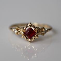 a gold ring with a red stone surrounded by white diamonds on a gray surface,