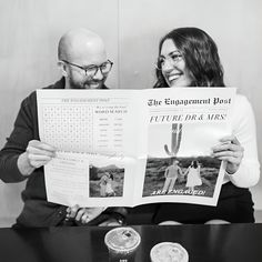 a man and woman sitting at a table holding up a magazine with pictures on it