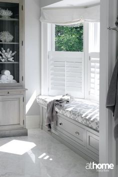 a bathroom with white tile floors and walls, along with an open window that has shutters