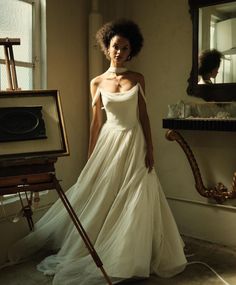 a woman in a white dress standing next to an easel