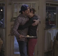 a man and woman kissing in front of an open door while holding a plate with food on it