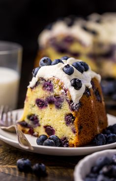 a slice of blueberry cake on a white plate with fork and glass of milk