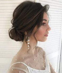 a woman in a white dress with pearls on her shoulder and hair styled into a low bun