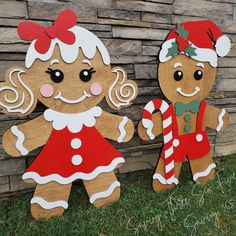 two wooden gingerbread man and woman standing next to each other in front of a brick wall