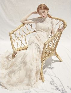 a woman is sitting on a wicker chair wearing a white dress and holding her hair