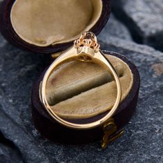 an open ring box sitting on top of a rock with a gold wedding band in it