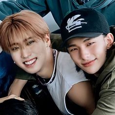 two young men posing for the camera with their arms around each other, one wearing a baseball cap