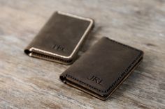 two personalized leather wallets sitting on top of a wooden table next to each other