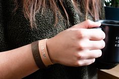 a woman holding a black coffee mug in her right hand and wearing a brown bracelet