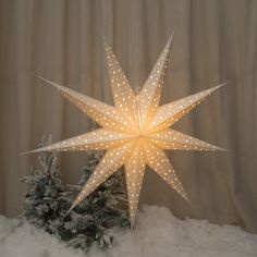 a lighted star ornament sitting on top of snow covered ground next to a christmas tree