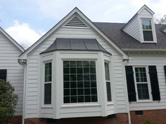 a white house with black shutters on the front and side windows in it's roof