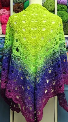 a crocheted shawl is displayed in front of many yarns on display