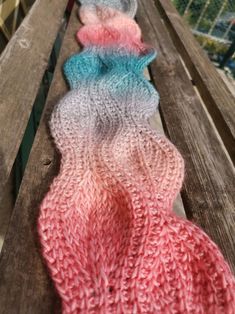 three knitted scarves sitting on top of a wooden bench