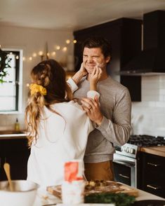 a man standing next to a woman in a kitchen while she wipes her nose