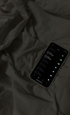 a cell phone laying on top of a bed covered in black sheets and blankets with green buttons