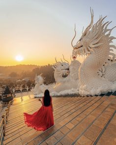 a woman in a red dress standing on a roof next to two white dragon statues