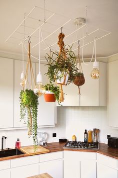 some plants hanging from the ceiling in a white kitchen with wooden counter tops and cabinets